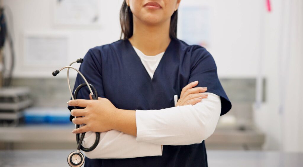 A close-up of a nurse with hands and arms crossed with a stethoscope in one hand, in a medical space